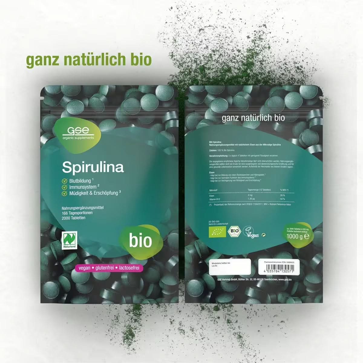 Abgebildet sind zwei grüne Packungen mit gse.organic.supplements Naturland Bio Spirulina (Tabletten) mit den Aufschriften „bio“ und „ganz natürlich“, dazwischen liegen verstreut vegane Tabletten. Auf der Verpackung steht, dass sie reich an Eisen, glutenfrei und laktosefrei sind (Informationen auf Deutsch).