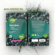 Abgebildet sind zwei grüne Packungen mit gse.organic.supplements Naturland Bio Spirulina (Tabletten) mit den Aufschriften „bio“ und „ganz natürlich“, dazwischen liegen verstreut vegane Tabletten. Auf der Verpackung steht, dass sie reich an Eisen, glutenfrei und laktosefrei sind (Informationen auf Deutsch).