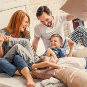 Eine fröhliche vierköpfige Familie, zwei Erwachsene und zwei Kinder, liefert sich eine lebhafte Kissenschlacht auf einem gemütlichen Bett, ihre Energie so lebendig wie CitroPlus® 1200 forte (Bio) von gse.organic.supplements.